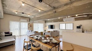 Un grand espace de vie comprenant une table à manger en bois, plusieurs chaises, un canapé et un téléviseur.