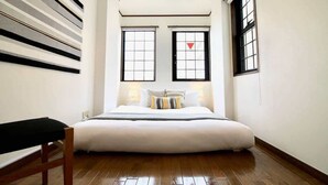 A bedroom with a large bed, two windows with black frames, a bench, and a wall with a geometric pattern. - Next to Peace Park, Convenient Central Stay P61 (Hiroshima City)
