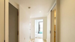 Un pasillo con piso de madera, una puerta a la izquierda y una cama con almohadas al fondo.
