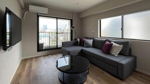 Una sala de estar moderna con un sofá modular gris, una mesa de centro redonda de vidrio y amplias ventanas con vista a la ciudad.