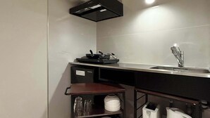 Een kleine keuken met een magnetron, waterkoker en een klein schap met servies.
