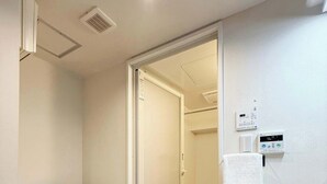 Een kleine badkamer met een witte wastafel, toilet, douche en wasmachine.