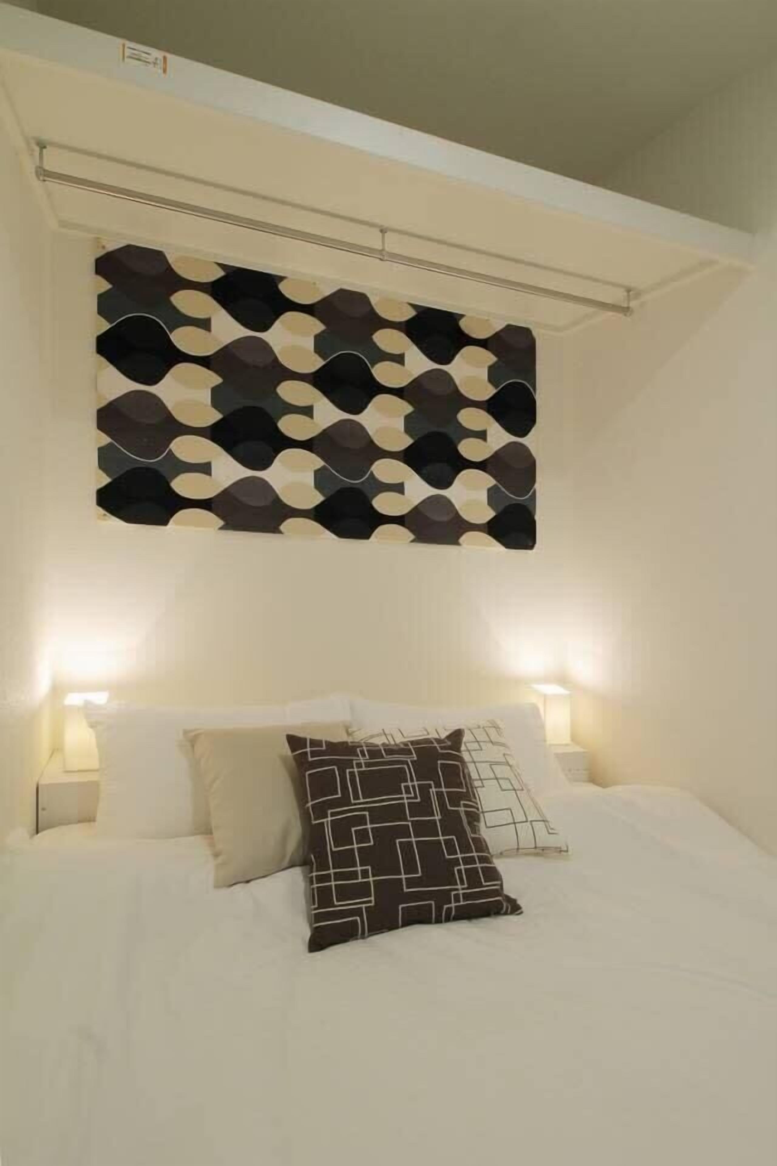 A neatly made bed with patterned pillows, a geometric wall decoration, and bedside lamps.