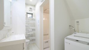 Ein modernes Badezimmer mit einem weißen Waschbecken, einer Toilette und einer Dusche. Die Wände haben ein helles Holzpaneel-Muster, und über der Toilette befindet sich ein Fenster.