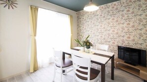 Un coin repas comprenant une table, des chaises, un téléviseur et un papier peint à motifs floraux.