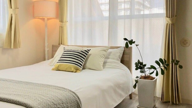 Un lit bien fait, avec un oreiller à rayures, une lampe de chevet et une plante en pot.