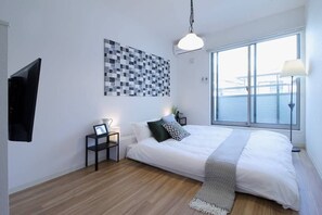 Ein modernes Schlafzimmer mit einem großen Bett, Blick auf das Wasser durch das Fenster, einem wandmontierten Fernseher und einem kleinen Nachttisch mit Lampe.