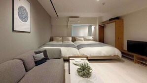A modern bedroom with a bed, a sofa, a TV, and a wall-mounted air conditioner. - ORIGAMINN 502 by b hotel - 5 mins PeacePark (Hiroshima City)