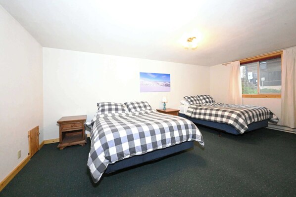 A room with two beds, a small wooden nightstand, a lamp, and a window with curtains.
