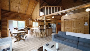Una cabaña de troncos con comedor, cocina y sala de estar con sofá.