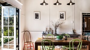 Un comedor con mesa de madera, sillas verdes, lámparas colgantes e imágenes enmarcadas en la pared.