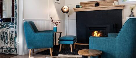 A cozy living room with teal armchairs, a small wooden table, and a fireplace.