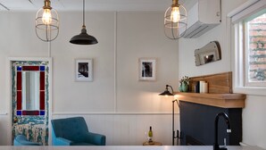 Una cocina moderna con luces colgantes, un sillón azul, encimera de madera y vista a un muro de ladrillo.