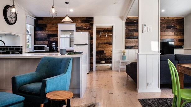 Una cocina moderna con una isla central, un comedor con sofá y sillas, y una sala de estar con televisor y asientos.