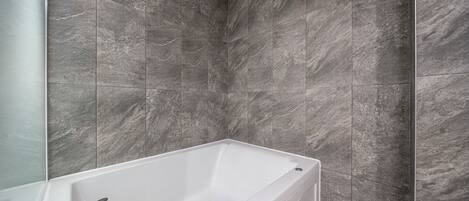 A modern bathroom with a white bathtub, grey marble tiles, and a chrome faucet.