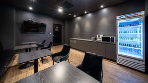 A modern restaurant with a dark interior, wooden flooring, and black chairs. There is a large refrigerator with beverages and a microwave on the counter. - Stay Month Hotel (Goyang)