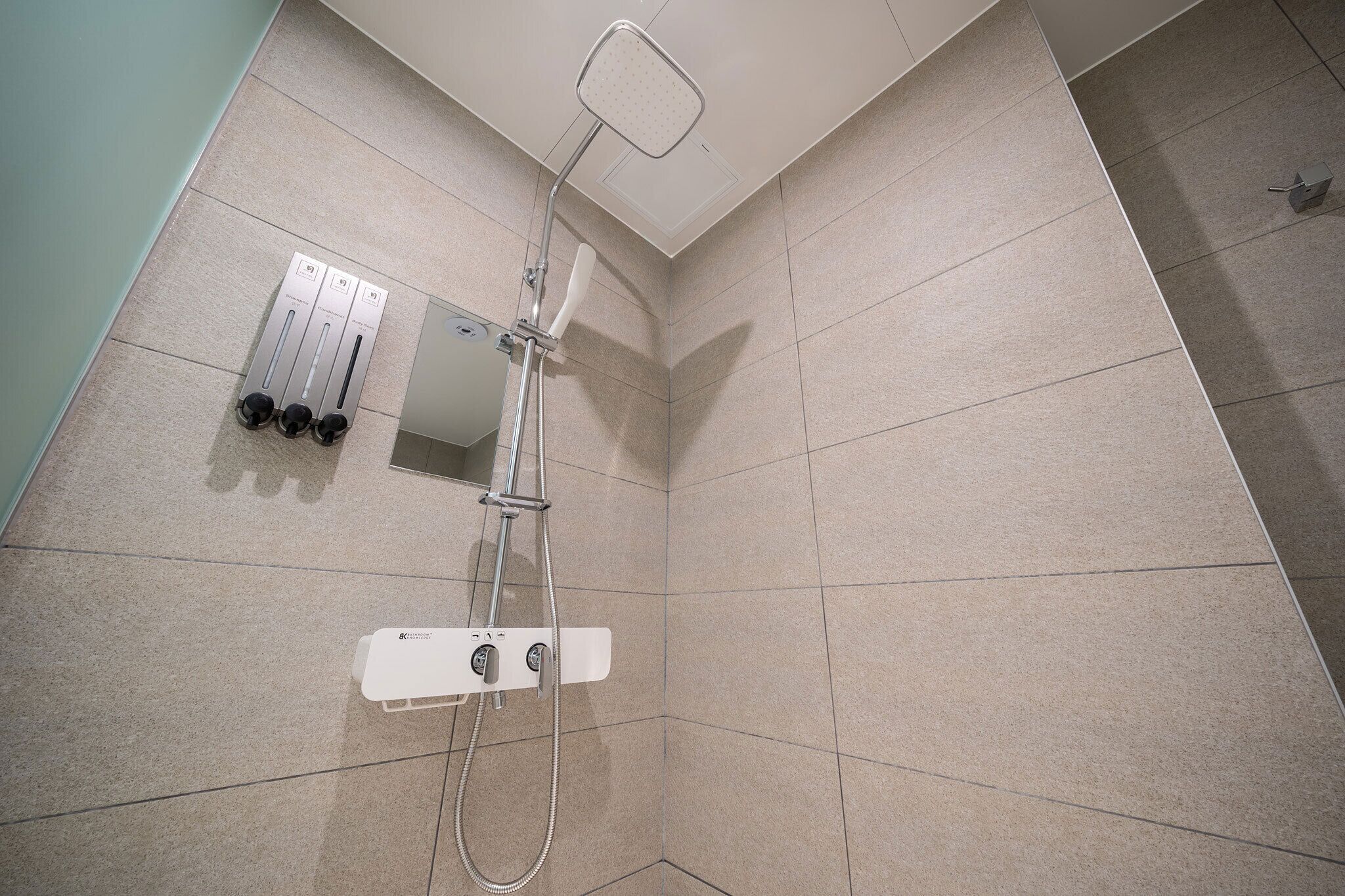 A shower with a handheld showerhead and a wall-mounted control panel.