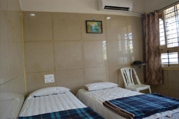 A room with two beds, a white chair, a window with curtains, and a wall-mounted air conditioner.