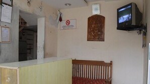 A room with a wooden bed, a television mounted on the wall, and a no-smoking sign. - Mourya Deluxe AC Lodge (Chitradurga)