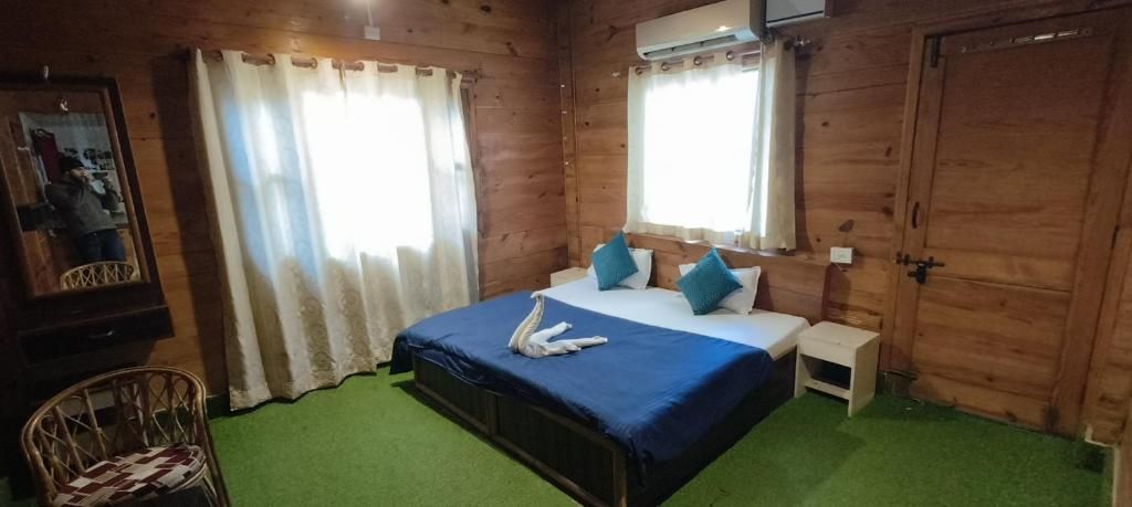 A wooden cabin-style room with a bed, a nightstand, a chair, and a window with curtains.