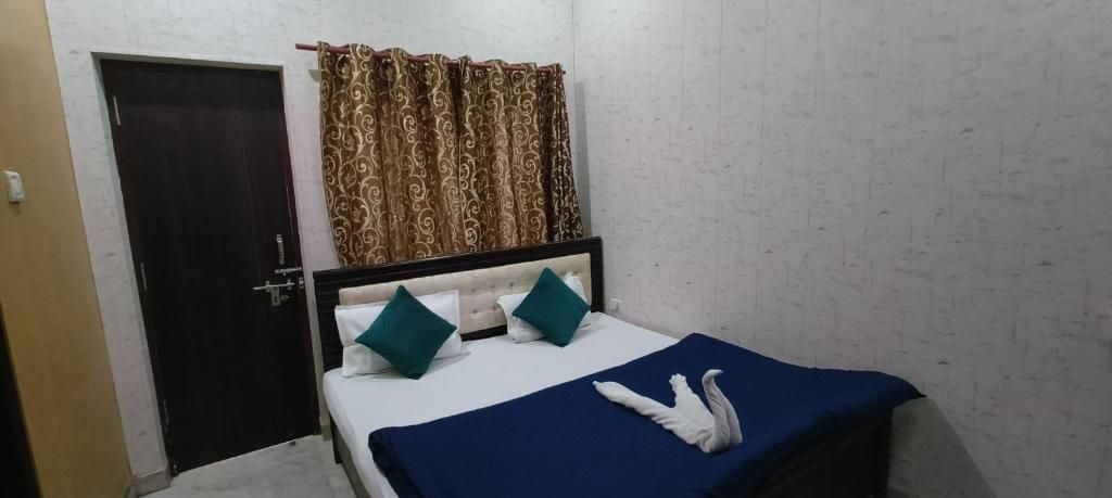 Een slaapkamer met een bed, twee kussens, een blauwe sprei, een witte zwaan decoratie, een deur en gordijnen met een patroon.