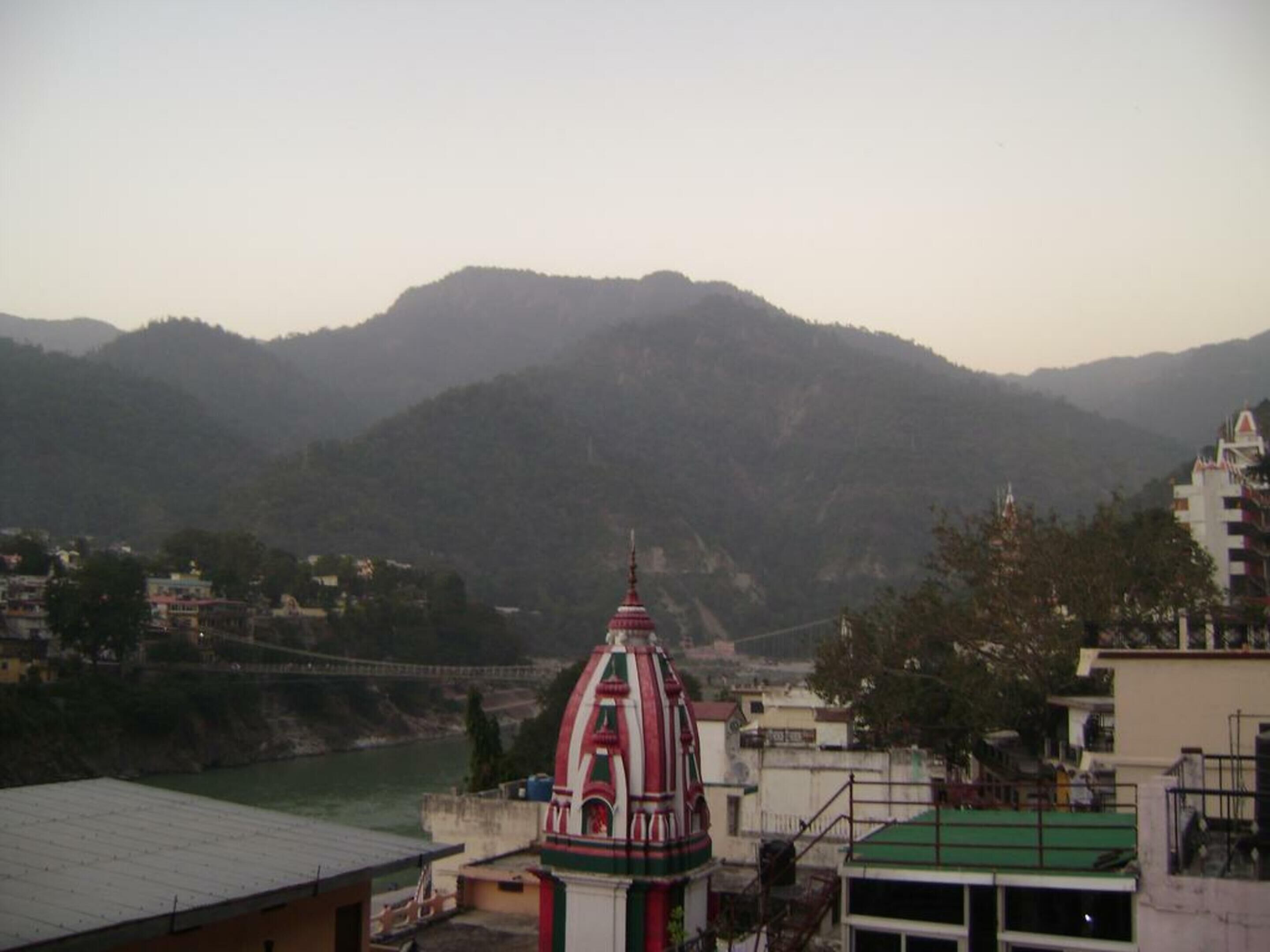 A view of a mountainous landscape with a river in the foreground and a temple with a red and white spire in the middle ground.