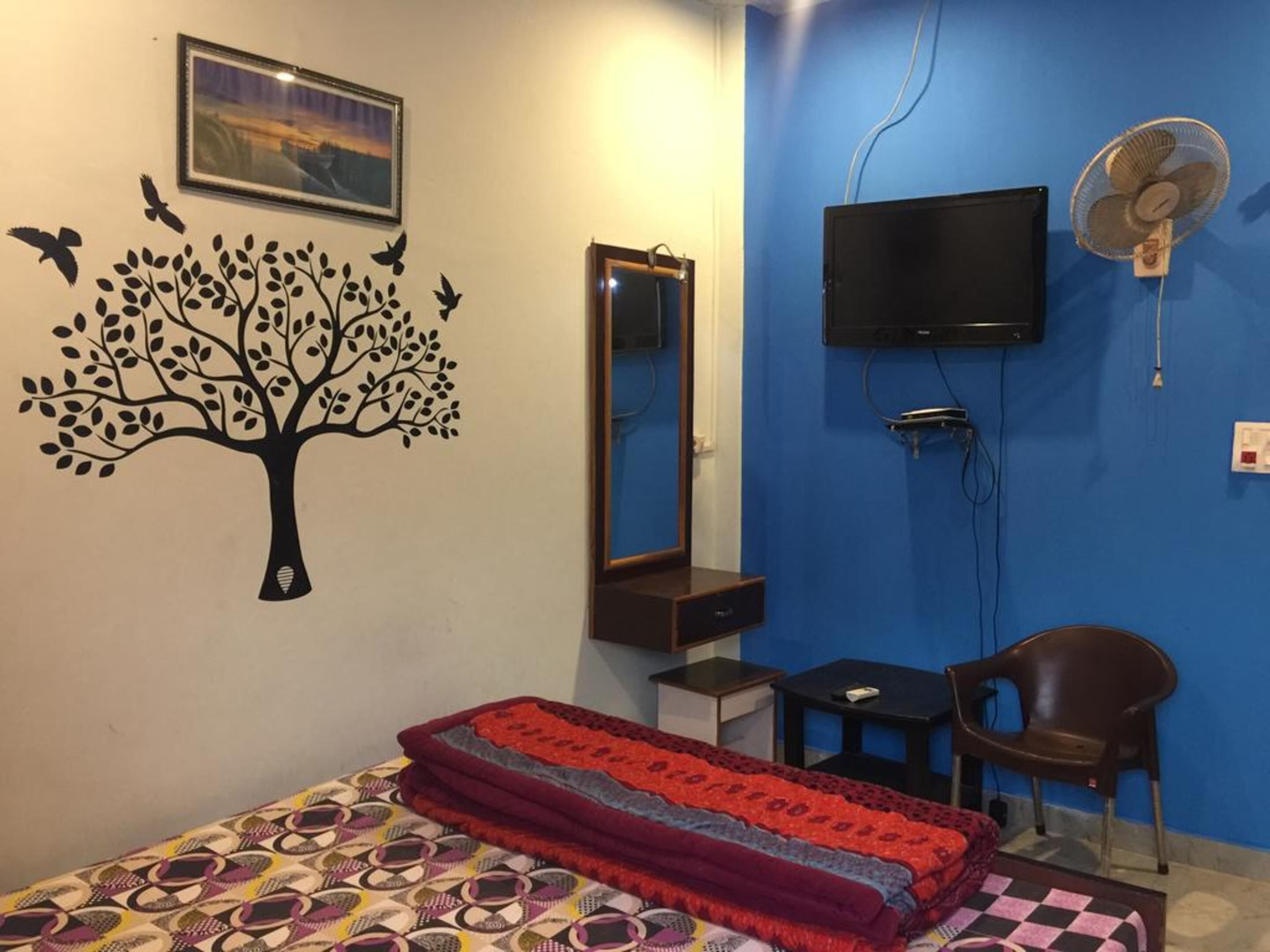 Une chambre à coucher comprenant un lit, une chaise, un téléviseur et un ventilateur fixé au mur.