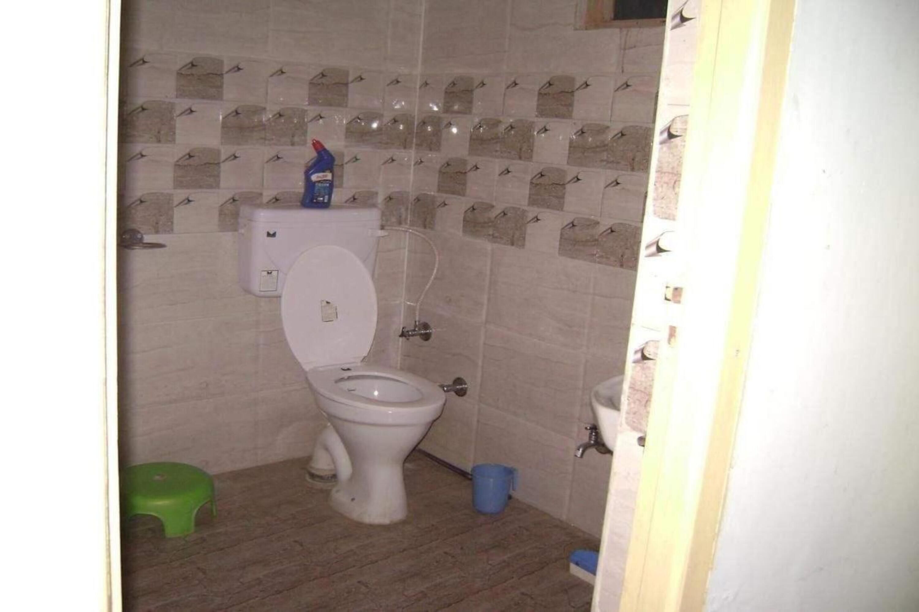 Un baño pequeño con un inodoro, un taburete verde y un cubo azul.