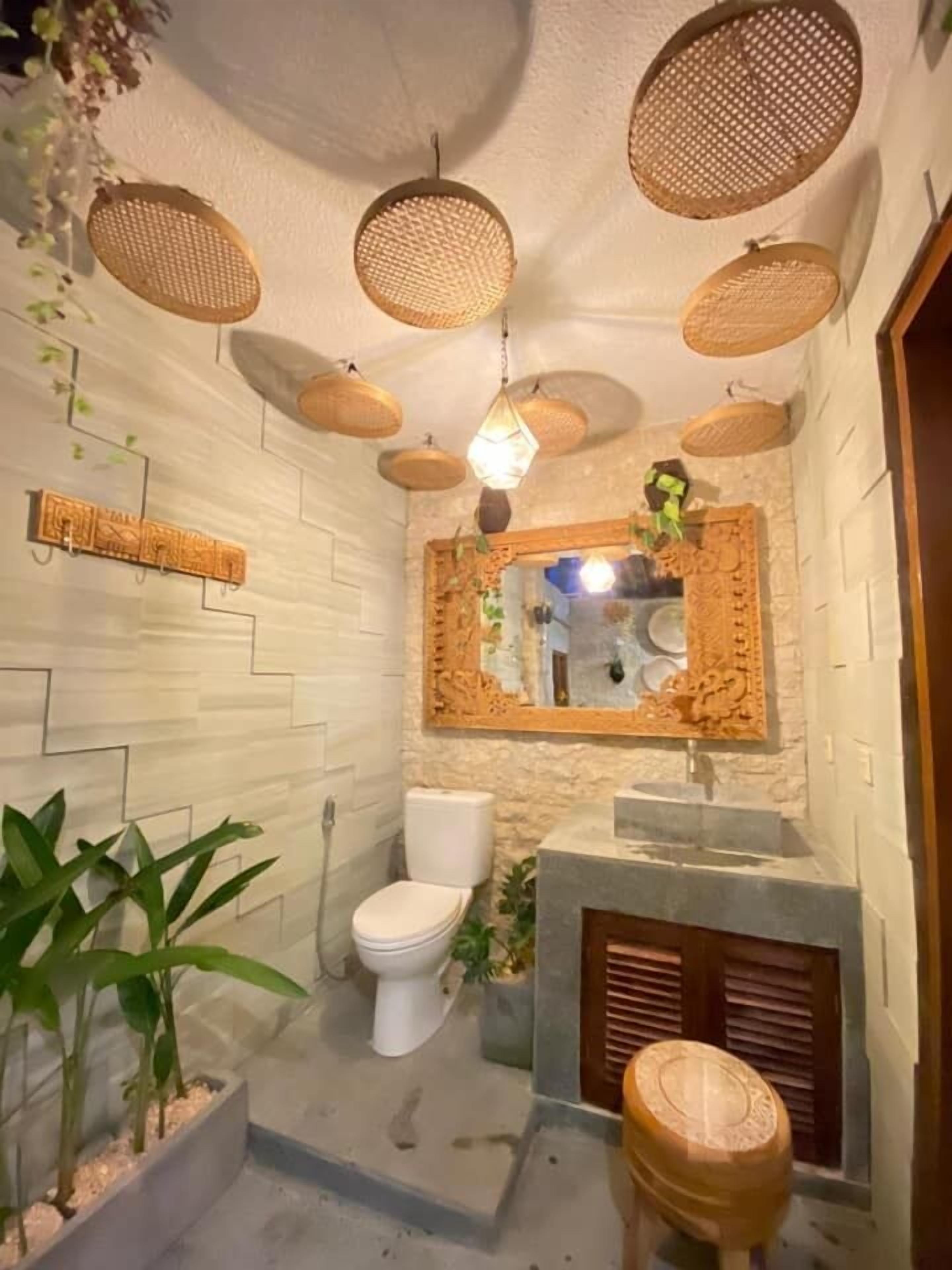 Une salle de bain avec un mur recouvert de carreaux blancs, des toilettes blanches, un lavabo avec un miroir au-dessus et un luminaire suspendu.