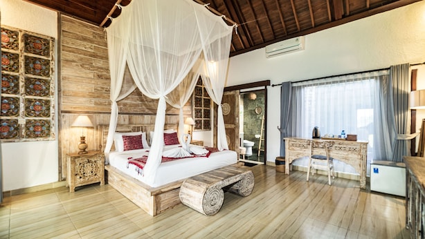 Un lit à baldaquin à quatre poteaux, avec un banc en bois, un bureau et une salle de bain visibles au fond.