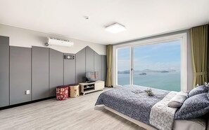 A modern hotel room with a large bed, a TV, and a view of the sea.