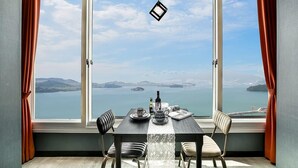 A dining area with a table set for two, overlooking a scenic view of a body of water and distant land. - Blooming Pension (Yeosu)