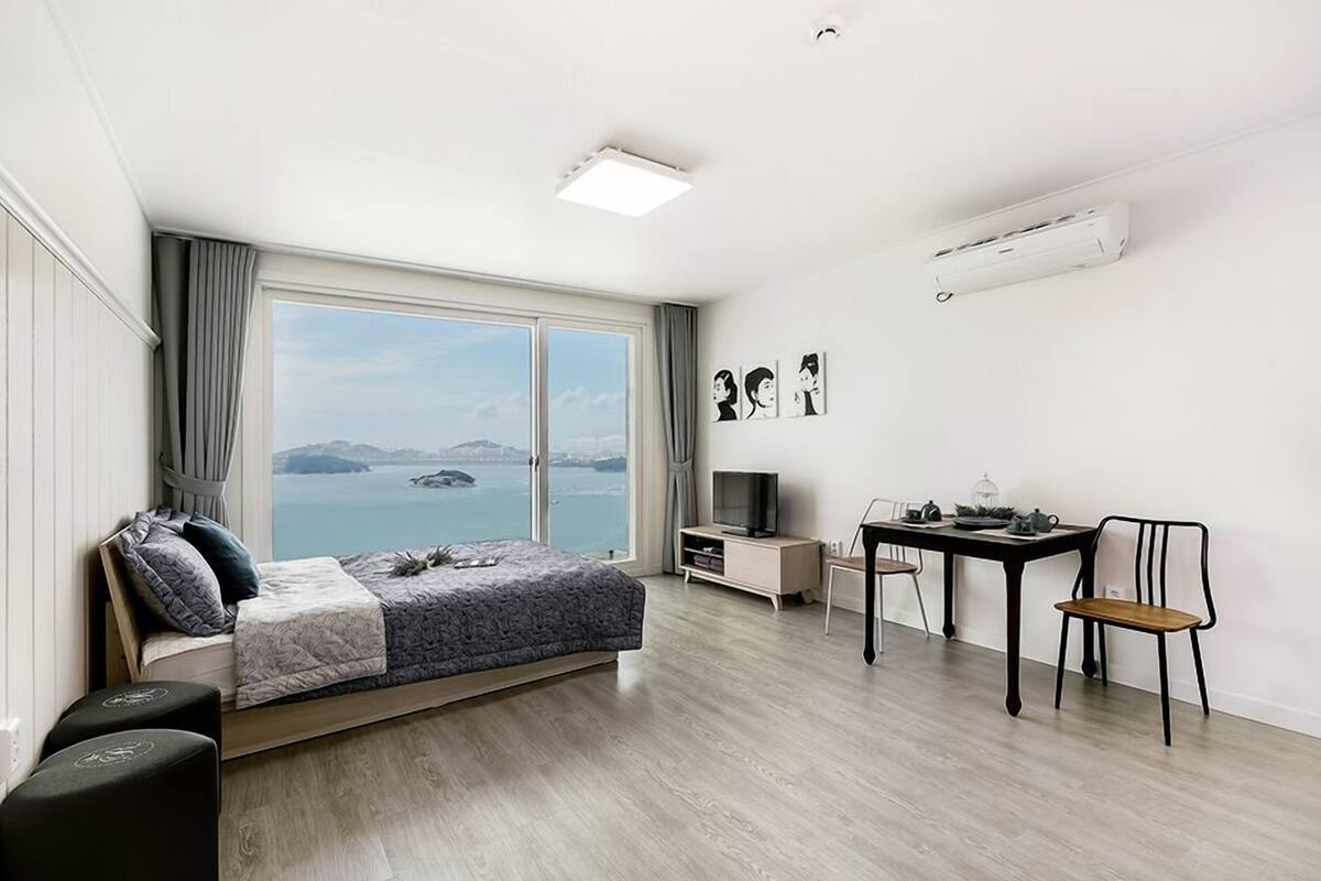 A modern bedroom with a large window, a bed, a desk, and a chair.