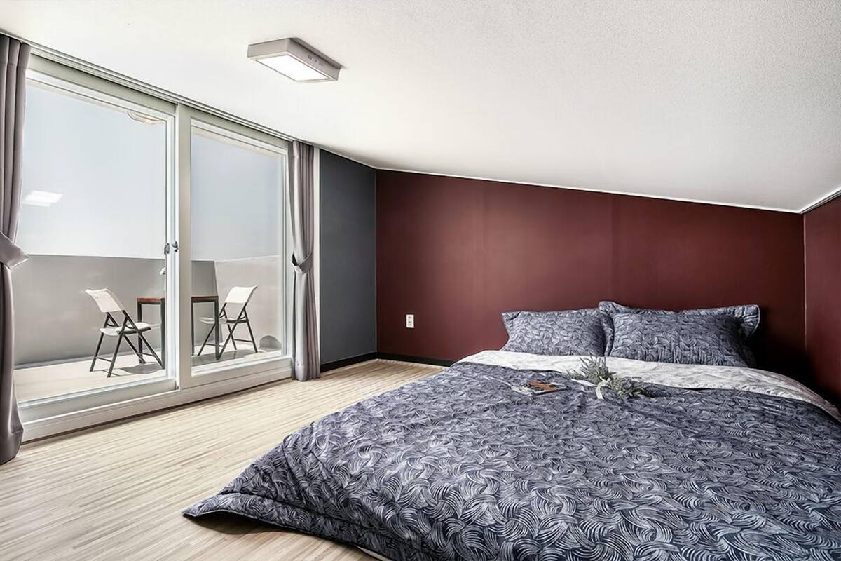 A modern bedroom with a large bed, a sliding glass door leading to a balcony, and a small seating area with chairs.