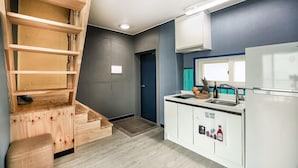 A modern kitchen with a wooden staircase, a sink, and a refrigerator. - Blooming Pension (Yeosu)