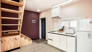 A modern kitchen with white cabinets, a stainless steel sink, and a built-in oven. There is a wooden staircase with a red wall on one side and a door leading to another room. - Blooming Pension (Yeosu)