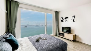 A bedroom with a large window, a bed, a TV, and artwork on the wall. - Blooming Pension (Yeosu)
