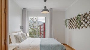 A modern bedroom with a bed, bedside tables, a hanging light fixture, a view through a glass door, and a wooden lattice wall decoration.
