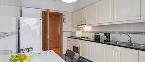 Una cocina moderna con armarios blancos, encimera negra y una zona de comedor con una mesa preparada para dos.