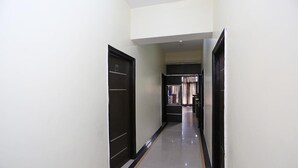 A hallway with black doors, white walls, and a yellow line on the floor. - Sunshine Residency (Noida)