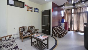 A living room with a sofa, two armchairs, a coffee table with magazines, a TV, and a patterned ottoman. - Sunshine Residency (Noida)