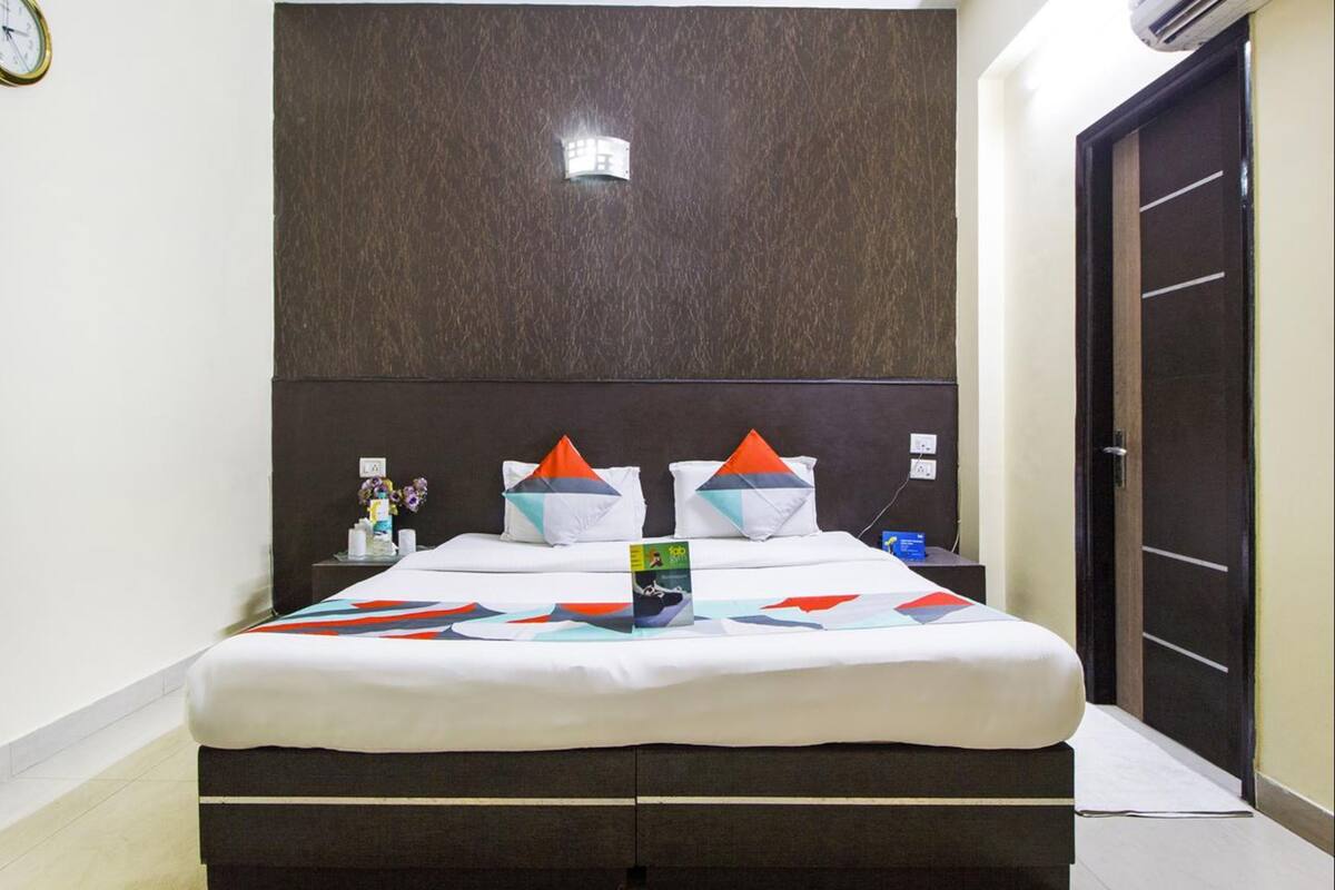 Una habitación de hotel con cama, mesita de noche, reloj y puerta.