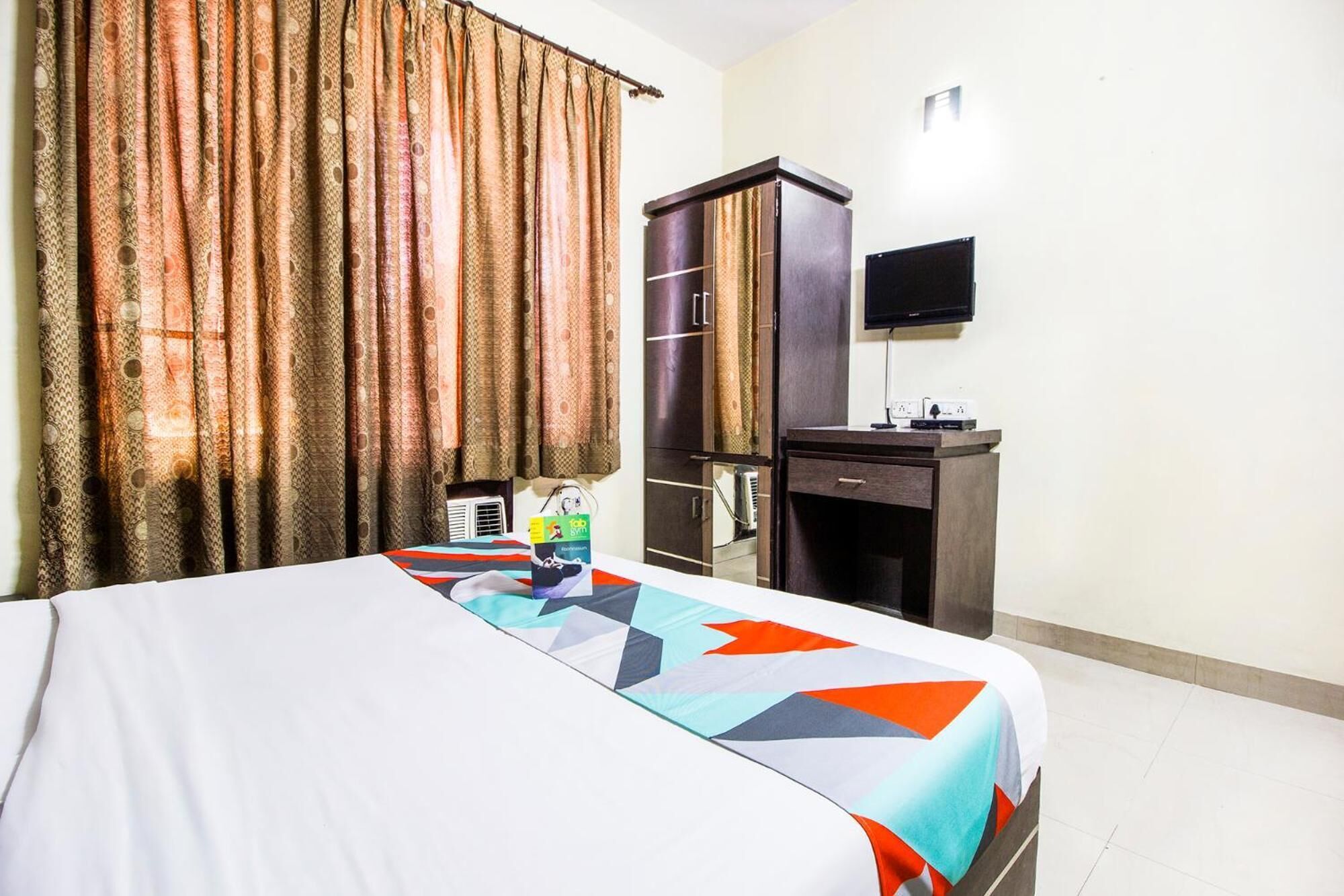 A hotel room with a bed, a desk, a television, and curtains.