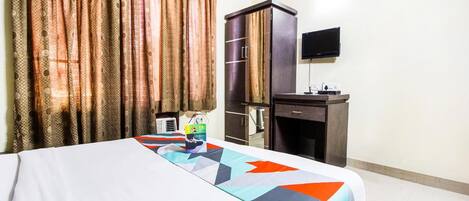 A hotel room with a bed, a desk, a television, and curtains.