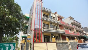 A multi-story residential building with a prominent vertical red glass structure, balconies, and a gated entrance. - Sunshine Residency (Noida)