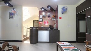 A reception area with a reception desk, a large fan, a staircase, and a patterned rug. - Sunshine Residency (Noida)