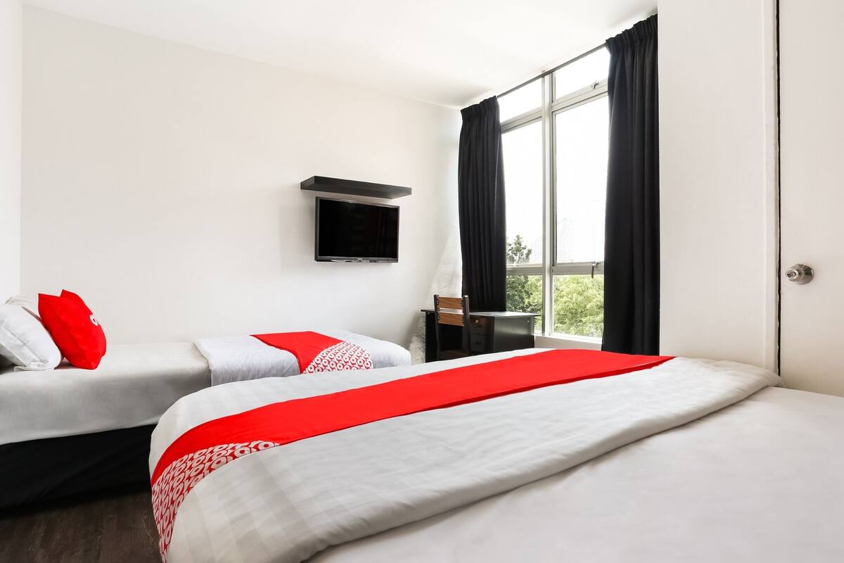 A hotel room with two beds, a TV mounted on the wall, and a window with black curtains.