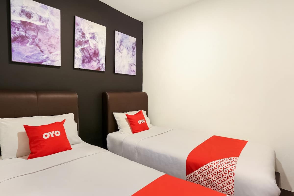 A hotel room with two beds, each with a white bedspread and red pillows. There are three abstract paintings on the wall above the beds.