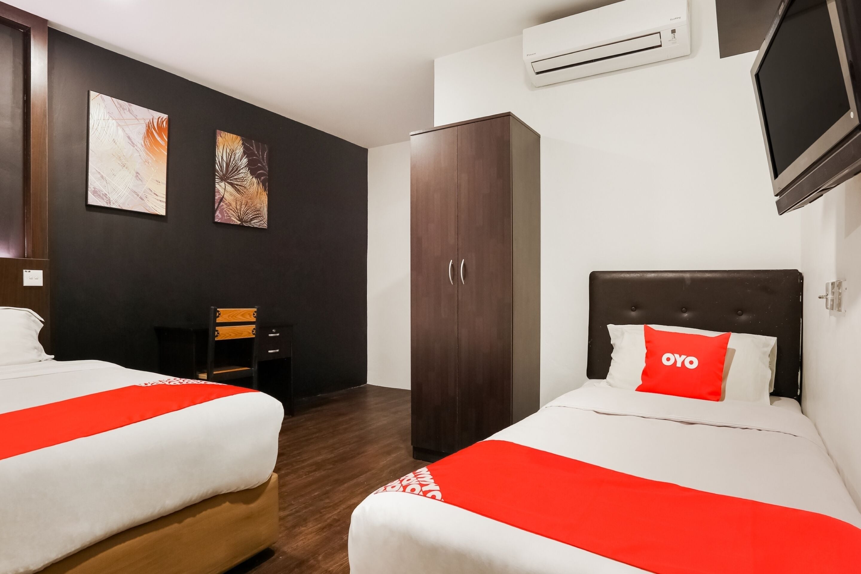 A hotel room with two beds, a wardrobe, a television, and artwork on the wall.