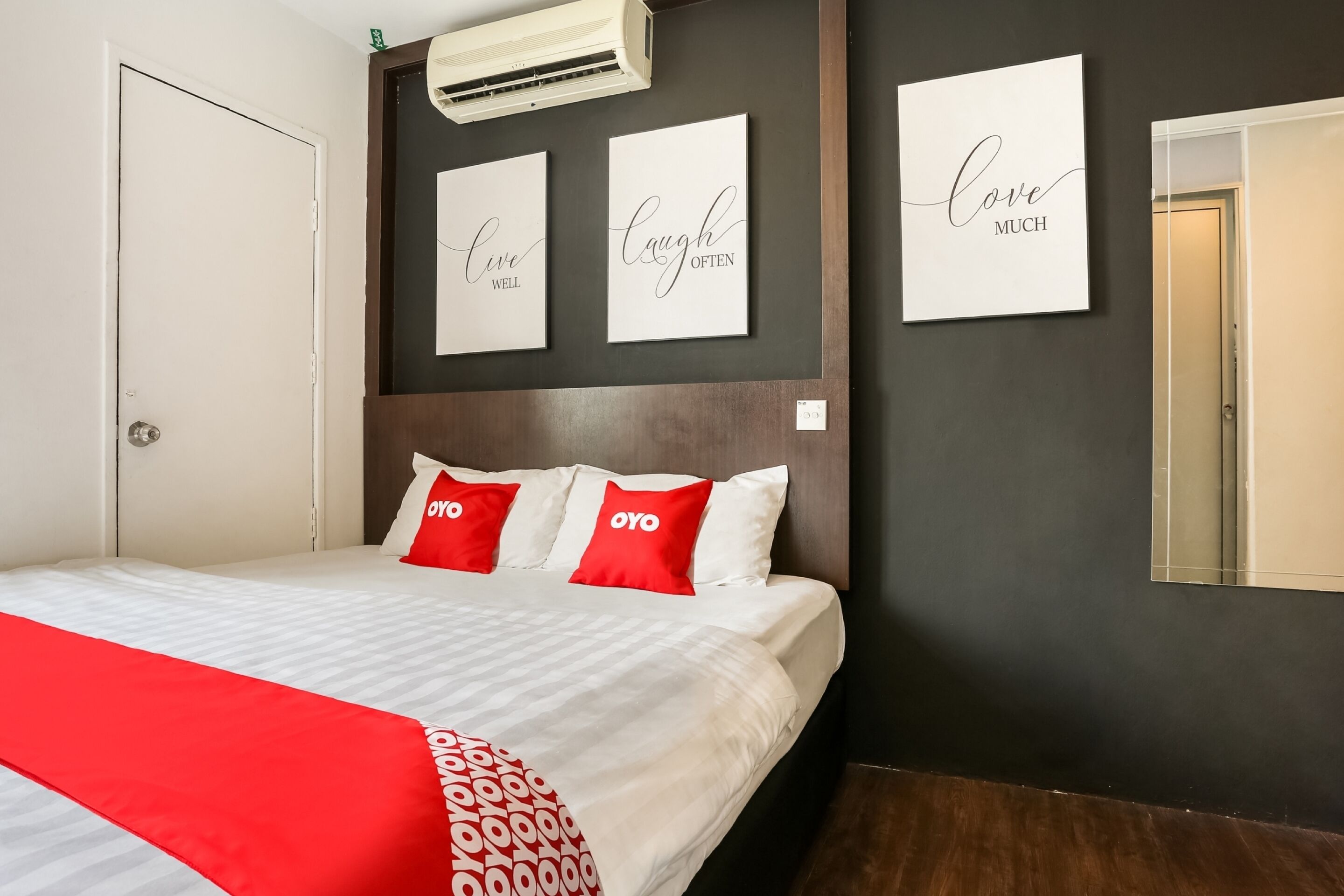 Ein Hotelzimmer mit einem Bett, einer roten Tagesdecke und drei Wandbildern mit motivierenden Sprüchen.